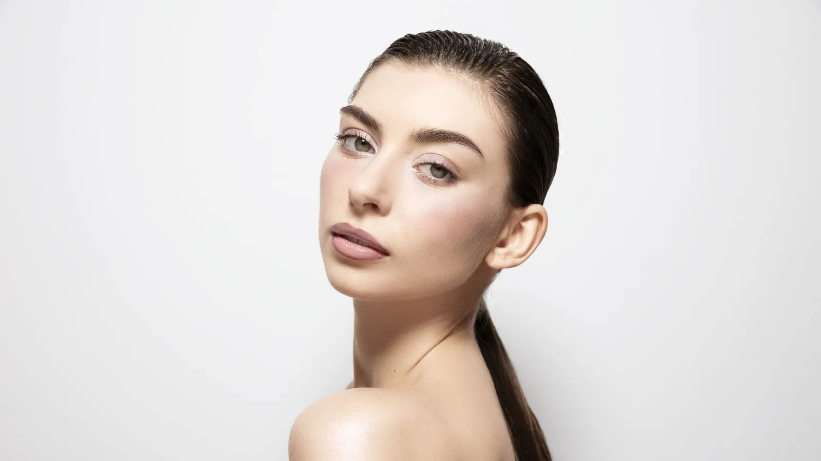 Eine junge Frau trägt dezentes Make-up. Ihre Haare sind in einem ordentlichen Zopf zusammengebunden, sodass das Make-up trotz seiner Schlichtheit im Vordergrund steht. Die Wangen sind leicht rosig. Die Lippen ebenfalls.